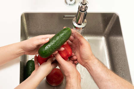 cucumbers and tomatoes are washed under running water in the sinkの写真素材