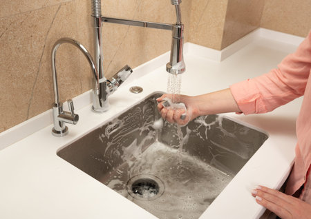 the girl washes away the foam in the kitchen sink from the sprayer faucetの写真素材