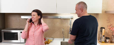 cute woman talking on the phone and man washing vegetablesの写真素材