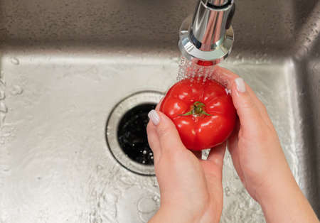 girls hands washing a tomato in the kitchenの写真素材