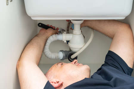do-it-yourself plumbing repair by a man under the sinkの写真素材