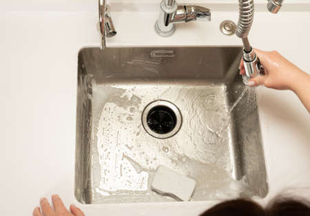 the girl washes away the foam in the kitchen sink from the sprayer faucetの写真素材
