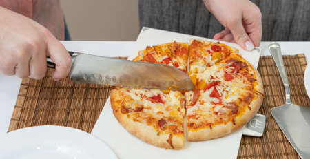 girl cuts homemade pizza with a knife on the tableの写真素材
