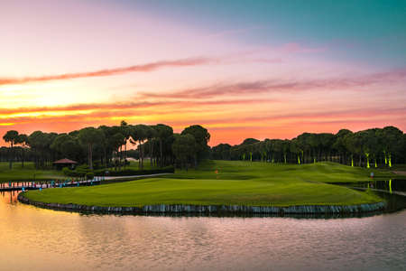 Panoramic view of beautiful golf course with pines at sunset. Golf field with fairway, lake and pine-treesの写真素材