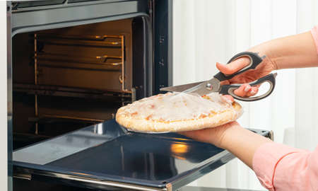 Womans hands with scissors cut a package of pizza close-upの写真素材
