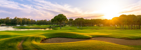 Golf course at sunset with beautiful sky and sand trap. Scenic panoramic view of golf fairway with bunker. Golf field with pinesの写真素材