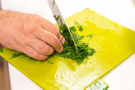 cutting dill with a kitchen knife male hands on a plastic cutting boardの写真素材
