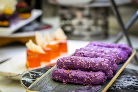 Eclairs with sweet purple topping with nuts on serving plateの写真素材