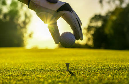 Closeup of golfer wearing glove placing golf ball on a tee at golf courseの写真素材