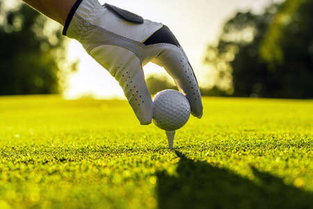 Hand of golfer wearing glove placing golf ball on a tee at golf course with sunlight on backgroundの写真素材