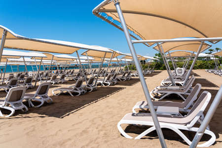 A rows of sunbeds at a deserted sandy beach in turkish resort. Sun loungers waiting for tourists in a hotelの写真素材