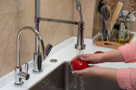 girls hands washing a tomato in the kitchenの写真素材