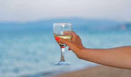 A glass of white wine in a womans hand against the backdrop of the sea. Close-upの写真素材