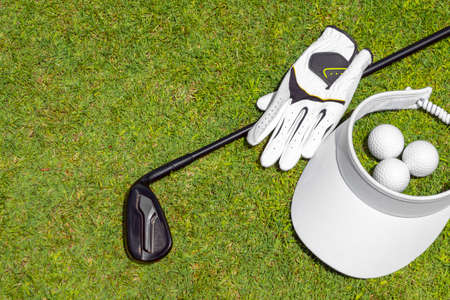 Top view of golf equipment on green grass on a golf course. Flat lay of golf club, balls, glove and capの写真素材