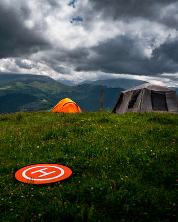 Camping in the mountains with tent standing on a hill, night and sunset landscape with helipad for droneの写真素材