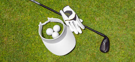 Top view of golf equipment on green grass on a golf course. Flat lay of golf club, balls, glove and capの写真素材