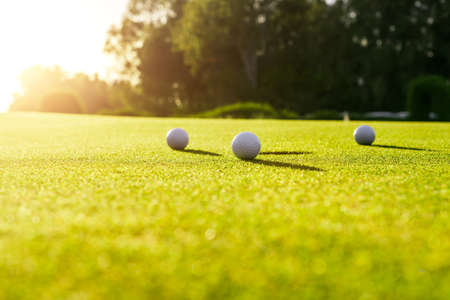 Three golf balls on the green grass near hole on a golf course at sunsetの写真素材