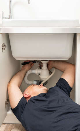 repairing a sink in a laundry room by an adult white male using toolsの写真素材