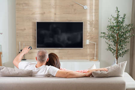 cheerful couple turns on the TV while lying on the sofa in the living roomの写真素材