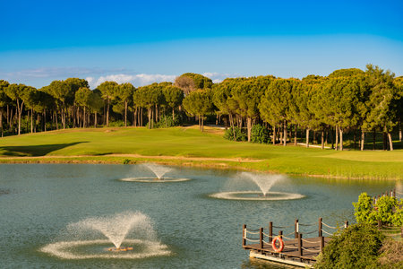 Golf course located behind the lake with fountainsの写真素材