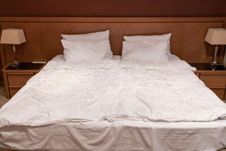 Close-up on a king size bed in a hotel room with bedside tables and lampsの写真素材
