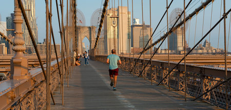 A man in shorts and a tank top is jogging on the Brooklyn Bridge