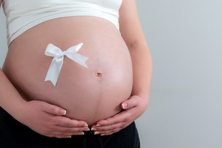Close-up of a beautiful female tummy in late pregnancy with a white bowの写真素材