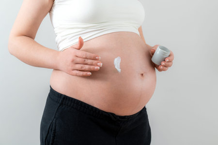 Pregnant woman applying cream on her belly for healing and skin elasticity