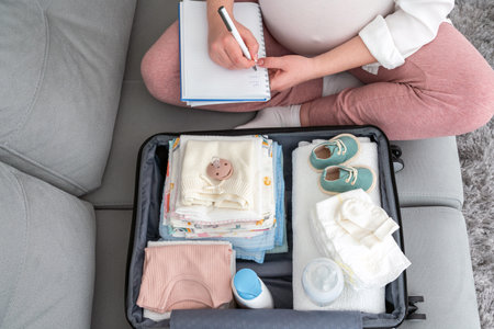 Pregnant woman at home, focused on writing a list, diligently packing suitcase for maternity hospital, embracing the future mother conceptの写真素材