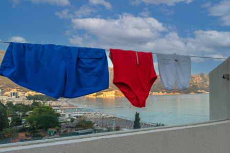 Colored swimsuits dry on the glass railing of a balcony overlooking a beautiful beachの写真素材