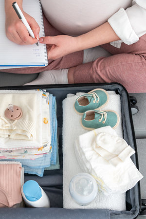 Pregnant woman at home, focused on writing a list, diligently packing suitcase for maternity hospital, embracing the future mother conceptの写真素材