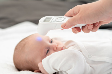 Mother ensures infants wellness with digital thermometer. Concept of advanced baby health monitoringの写真素材