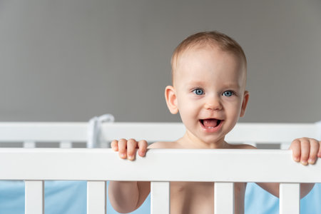 Baby girl with blue eyes standing in crib smilingの写真素材