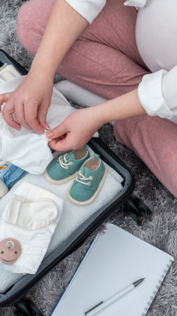 Pregnant woman from top view, diligently packing suitcase on the floor, preparing for maternity hospital, evoking future mother sentimentsの写真素材