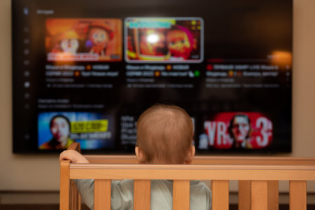 The baby watches a large TV from a crib. Concept of knowledge of the worldの写真素材