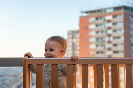 baby smiling cheerfully looks out of the crib against the backdrop of the city landscapeの写真素材