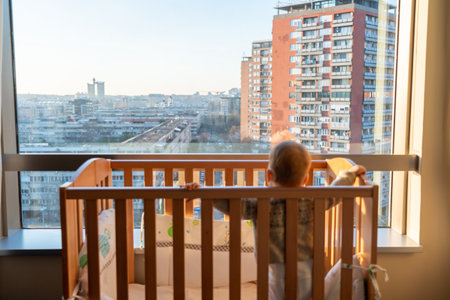 Baby looking out the panoramic window while standing in a cribの写真素材