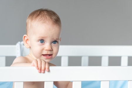 Baby with a vaguely distorted facial expression in a white classic cribの写真素材