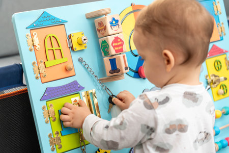 A toddler uses a key for a small lock while playing with a busy boardの写真素材