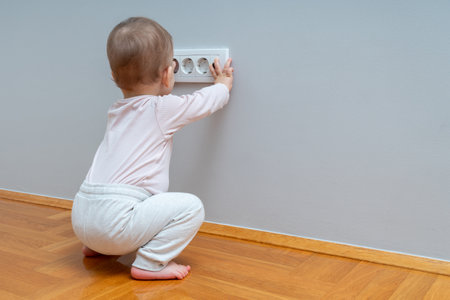 Baby hand reaching for an electrical outlet covered with safety plugsの写真素材