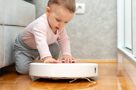 Baby tries to climb on robot vacuum cleaner. Concept of interaction with smart devicesの写真素材