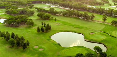 Golf course at sunset with pond and sand traps. Scenic panoramic view of golf fairway with bunkers. Golf field with pinesの写真素材