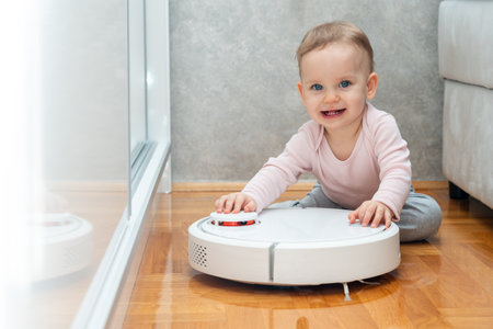 A toddler tries to hold a working robot vacuum cleaner in place. Concept of interaction with smart devicesの写真素材