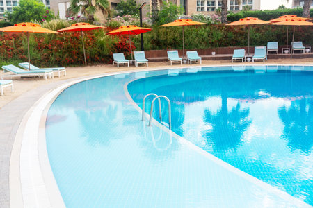 Step into a luxurious pool with a strip of coastal sand and brightly colored umbrellas and sun loungersの写真素材