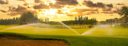 Golf course in maintenance. Watering golf course with sprinklers. Golf course at sunset.の写真素材