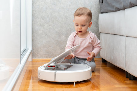 A toddler tries to get a garbage container out of a robot vacuum cleaner. Concept of learning about surrounding objectsの写真素材