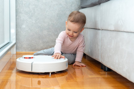 Baby tries to turn on robot vacuum cleaner. Household help conceptの写真素材