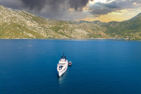Beautiful yacht with a small boat moored in a bay against the background of morning cloudsの写真素材