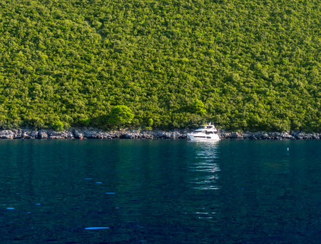 Small yacht or boat in bright blue sea against green cliffの写真素材