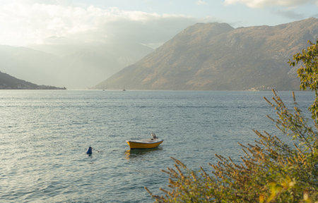 Tranquil Yellow Boat Floating on Serene Sea Amid Majestic Mountain Sceneryの写真素材